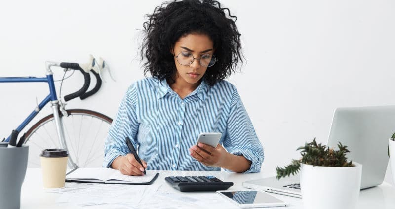 a woman looking at a phone while writing in a notebook