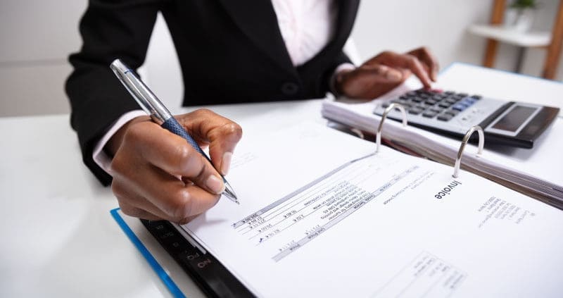 A person writing in a binder with invoices