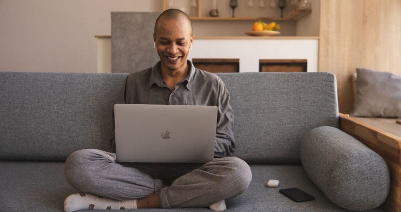 a person sitting on a couch while working on a laptop