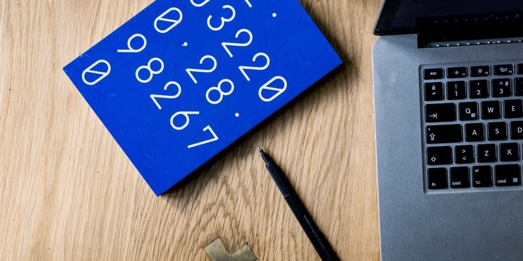 A blue notebook with numbers onthe cover rest on table near a laptop
