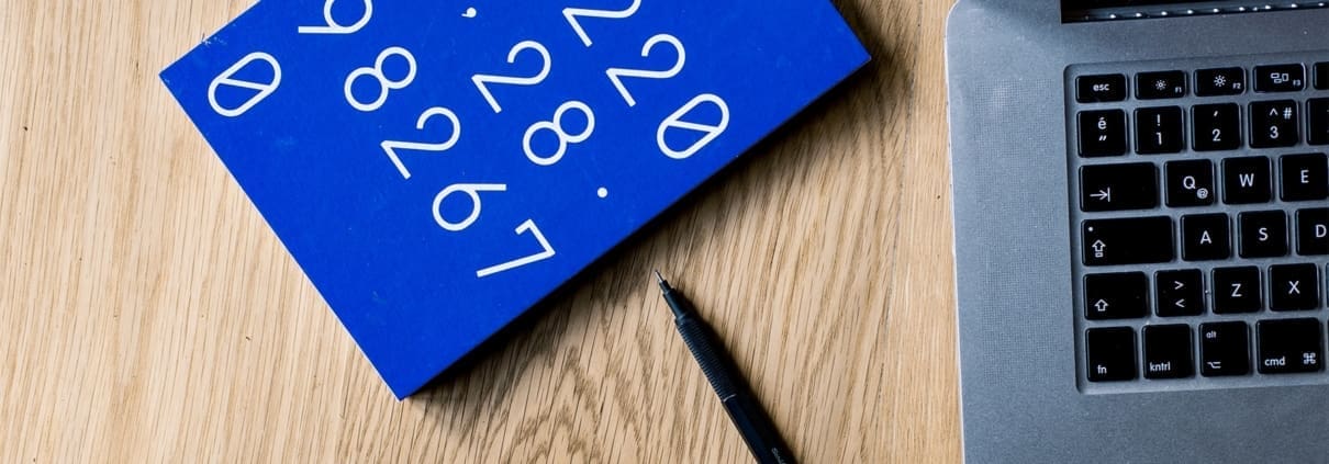 A blue notebook with numbers onthe cover rest on table near a laptop