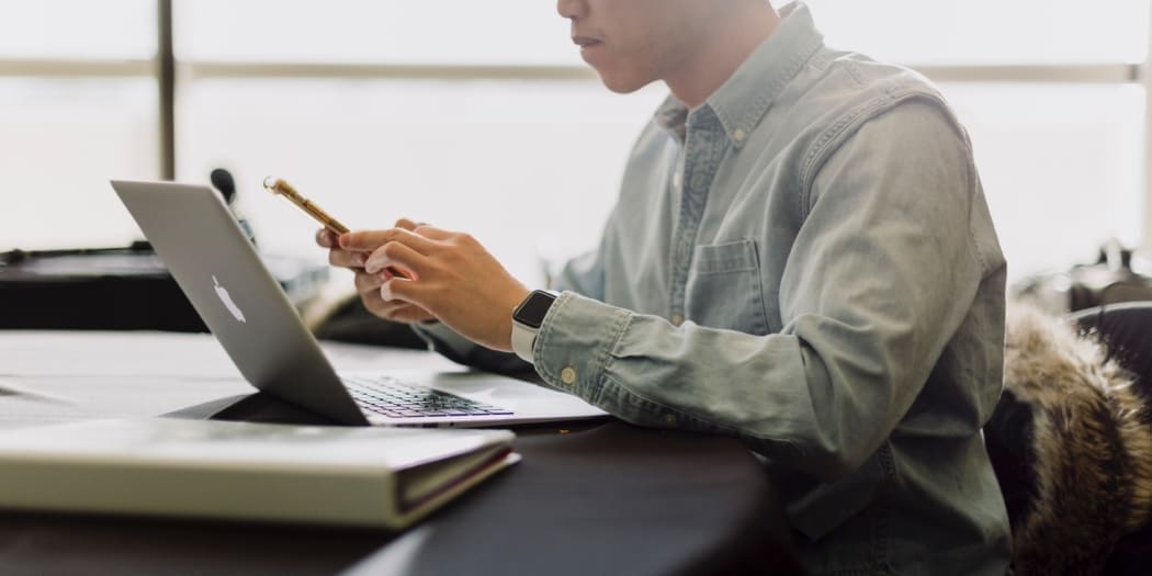 A man in an oxford shirt looks at his bookkeeping on his laptop