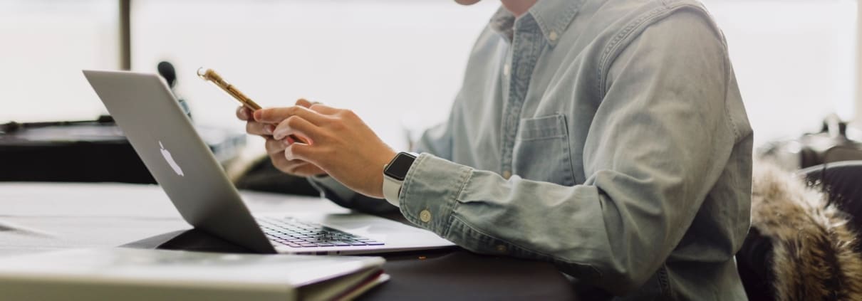 A man in an oxford shirt looks at his bookkeeping on his laptop