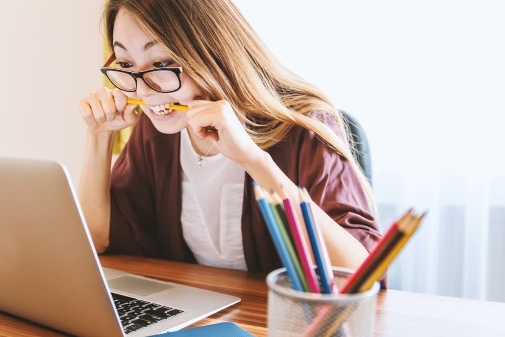 A woman sitting at her computer bites a pencil due to stress