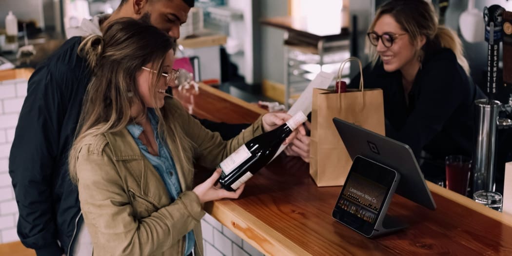 A restaurant worker helps two customers purchase wine