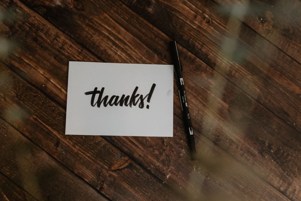 A hiwte thank you note with black cursive writing sits on a table