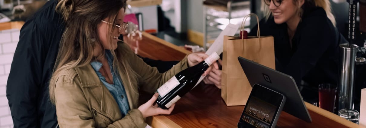 A restaurant worker helps two customers purchase wine