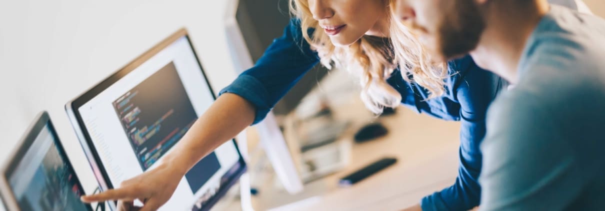 White female business over pointing at a computer and speaking to her white male employee