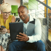 Black male business owner and white female business owner looking at a tablet, discussing business performance