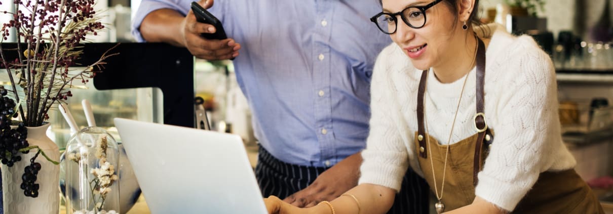 White female business owner and black male business owner using a laptiop, looking happy about business performance