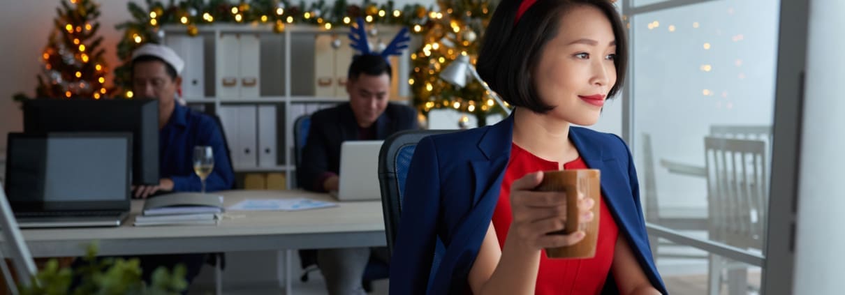 Smiling young Asian business owner working on computer and drinking coffee during the holidays