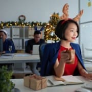 Smiling young Asian business owner working on computer and drinking coffee during the holidays