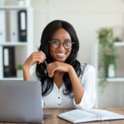 Portrait of cheerful black business lady sitting at her desk with laptop, smiling at camera in office. running her small business