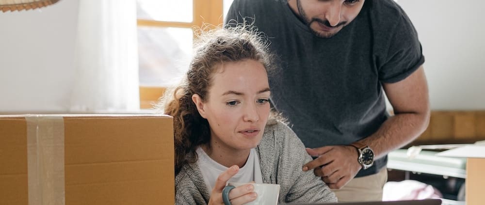Two people surrounding by boxes look at a computer