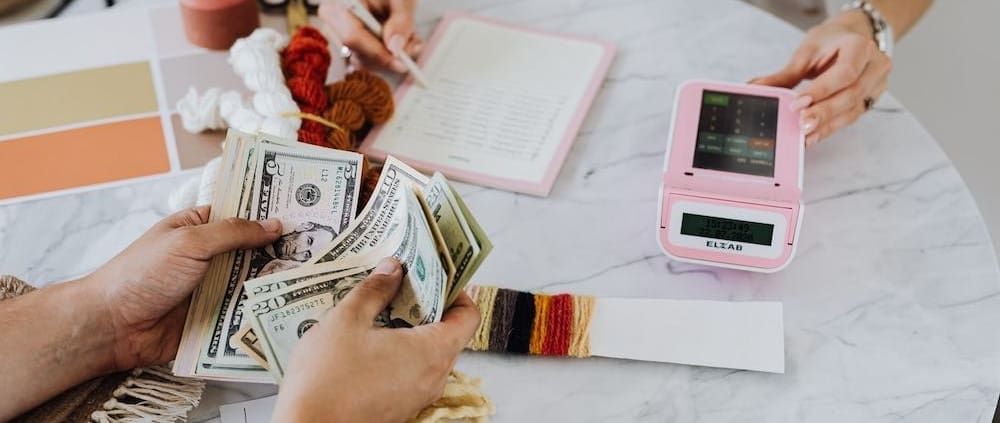Two people counting money and writing amounts on paper