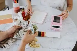 Two people counting money and writing amounts on paper