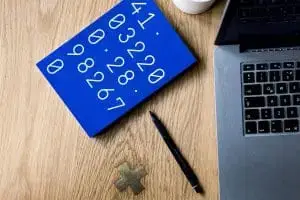 A blue notebook with numbers onthe cover rest on table near a laptop