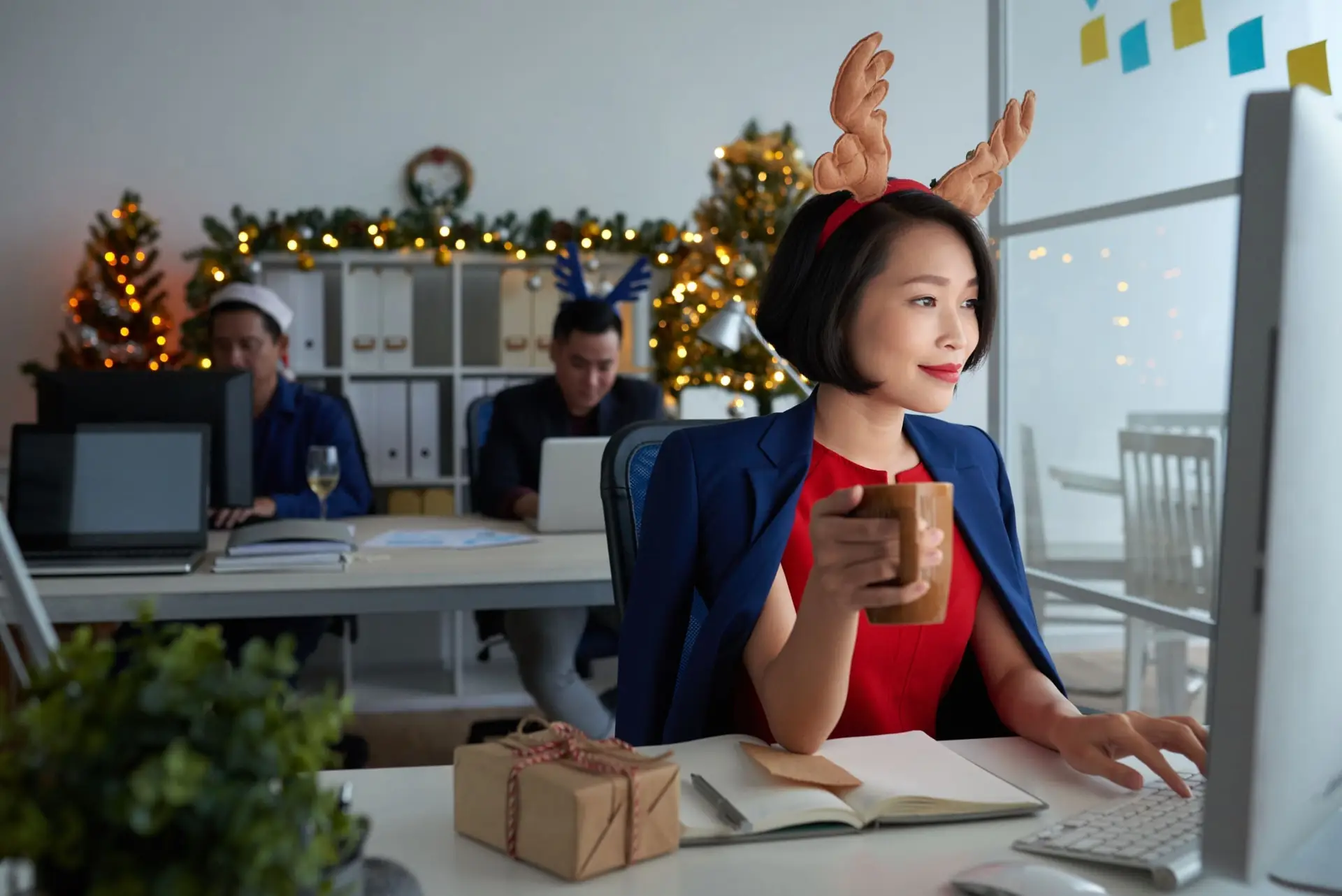 Smiling young Asian business owner working on computer and drinking coffee during the holidays