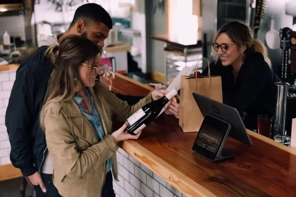 A restaurant worker helps two customers purchase wine