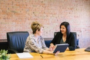 Two business woman smile discuss accounting at a desk|Two business women discuss Florida tax laws